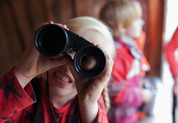 Flicka i förskolan tittar in i kameran via en kikare. Foto: Lo Birgersson